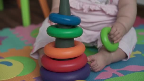 Bebé, concepto de la infancia - primer plano de sonriente feliz regordete divertido niño gordito recién nacido despierto niña de 8 meses sentarse gatear en juego de piso estera con pirámide multicolor en la sala de juegos en el interior de casa — Vídeos de Stock