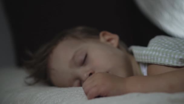 Расслабление, сладкие сны, детство, семейные конфузы - маленькая двухлетняя дошколята мокрый мальчик спит на белой кровати, покрытой одеялом, в темной комнате в обеденный перерыв — стоковое видео