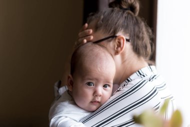 Çocukluk, annelik, hastalıklı aile kavramları - üzgün, sinirli iş kadını kadın baş ağrısı çeken anne yeni doğmuş bebeği elinde tutuyor evde pencerenin yanında duruyor
