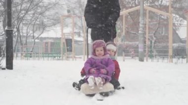 Kış, çocukluk, babalık, oyunlar, aile kavramları - iki mutlu anaokulu çocuğu kardeşler kızakla kayıyor çocuklar babalarıyla birlikte eğleniyor açık havada kar yağışı mevsiminde soğuk havada parkta oynuyorlar.