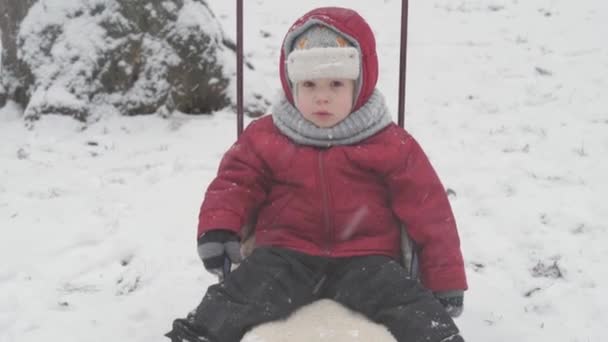 Детство, отцовство, игры, семейные концепции - закрыть один грустный, расстроенный ребенок дошкольного ребенка младший мальчик мальчик сын в теплой зимней одежде сани сидеть на санях в снегопад холодная погода в парке на открытом воздухе — стоковое видео