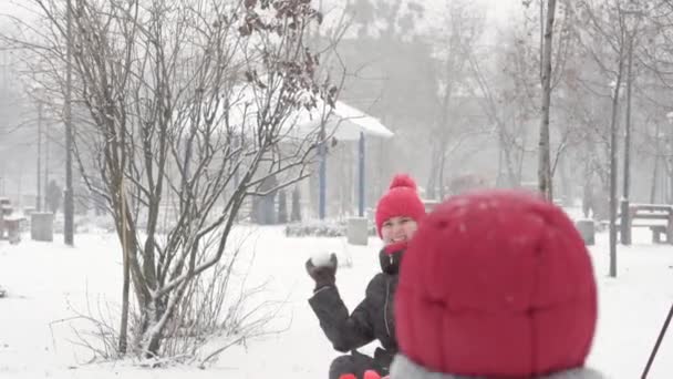 Inverno, férias, jogos, conceitos de família - Duas crianças pré-escolares felizes irmãos crianças vestidos com chapéus e luvas com a mãe jogando se divertir fazer bola de neve na queda de neve em tempo de estação fria no parque — Vídeo de Stock