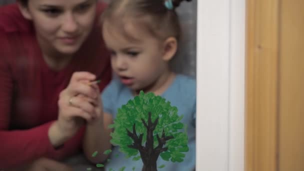 Enfance, maternité, créativité, nature, art, printemps, concept d'été - plan moyen de la jeune maman avec une petite fille de 3-4 ans dessiner sur verre de fenêtre. femme et préscolaire fille arbre à peinture. — Video