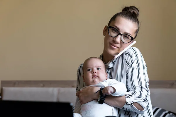 Childhood, motherhood, family concepts - successful smiling rich business woman Lady mother sit on bed with infant child baby talking on phone working on lap top computer at home in distance indoors