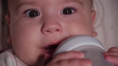 bebek, çocukluk, duygu konsepti - Kahverengi gözlü, yeni doğmuş, dişsiz bir bebeğin aşırı yakın plan gülümsemesi 7 aylık şişeden su içmesi ve bebek arabasında beyaz bir vücut giysisi içinde yatması
