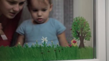 Çocukluk, annelik, yaratıcılık, doğa, sanat, bahar, yaz konsepti - 3-4 yaşlarında küçük kızı olan genç bir annenin pencere camına çizimi. Kadınlar ve anaokulu kızları çiçek boyarlar.