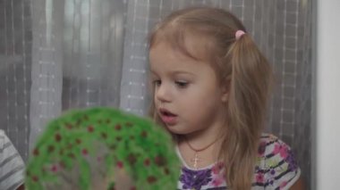 Çocukluk, yaratıcılık, doğa, ilkbahar, yaz konsepti - pencere camına akrilik renk çizen iki küçük anaokulu çocuğunun yakın çekimi. Kardeşlerin çocukları ve kız kardeşlerin manzara resimleri: ağaç, çimen