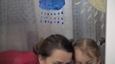 Çocukluk, annelik, yaratıcılık, doğa, sanat, bahar, yaz konsepti - 3-4 yaşlarında küçük kızı olan genç bir annenin pencere camına çizimi. kadın ve anaokulu kızı ağaç boyuyorlar..