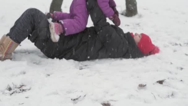 Tél, nyaralás, játékok, családi fogalmak - boldog óvodai kisgyerek lánya lány menekülni játszik, hogy hógolyó hó angyalok anya elesik, feküdt a hóesésben hideg évszak időjárás a parkban szabadban — Stock videók