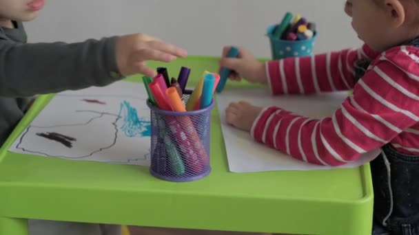 Kunst, onderwijs, kindertijd, concepten - Kleine gelukkige slimme kleuter kleuter broertje en zusje kinderen tekent met viltstiften en potloden zitten binnen aan tafel. glimlachende kinderen broer zus schildert binnen — Stockvideo