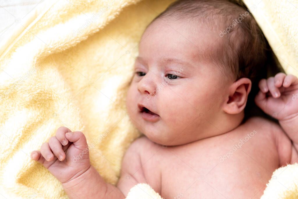 Childhood, care, hygiene, motherhood, innocence concepts - Close up Wet awake Infant newborn after taking shower wrapped in warm yellow towel looking at camera sucks tiny fingers. babys first bath