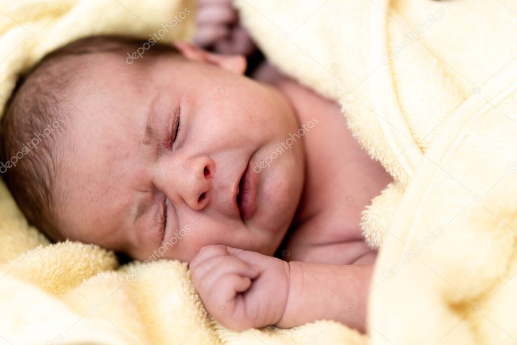 Childhood, care, hygiene, motherhood, innocence concepts - Close up hungry awake Infant newborn after taking shower wrapped in warm yellow towel cry close eyes sucks tiny fingers. babys first bath