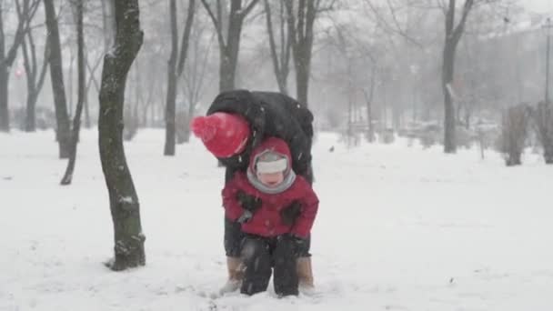 Zima, dovolená, hry, rodinné koncepty - šťastný školka batole dítě syn dítě chlapec utéct hrát, aby sněhová koule s mámou, baví točit kolem v sněžení chladné období počasí v parku venku. — Stock video