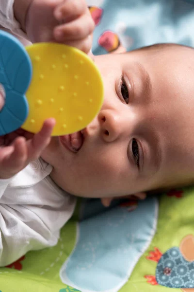 Infância, felicidade, conceitos de maternidade - Infante surpreendido, bebê recém-nascido engraçado com idades entre 3-4 meses brincando com brinquedos, roendo palitos de dentes no tapete de desenvolvimento deitado no estômago em casa dentro de casa — Fotografia de Stock