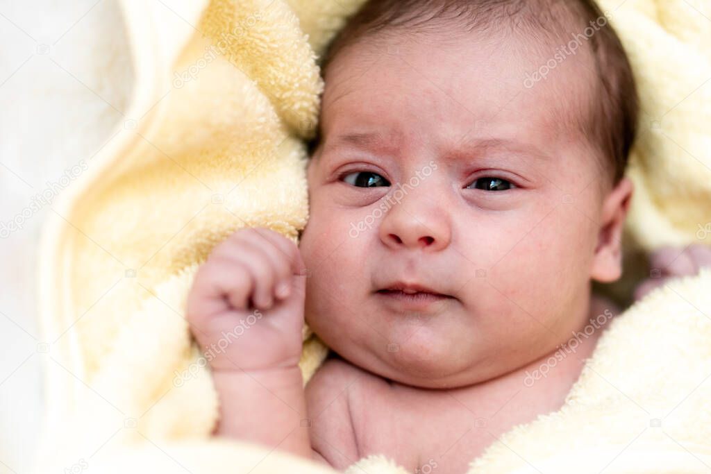 Childhood, care, hygiene, motherhood, innocence concepts - Tight Close up Wet awake Infant newborn after taking shower wrapped in warm yellow towel look at camera sucks tiny fingers. babys first bath