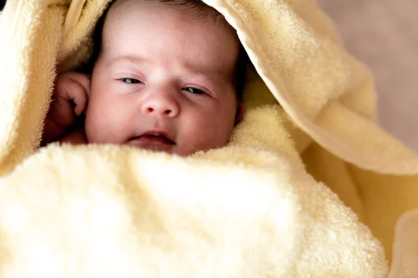 Детство, уход, гигиена, материнство, невинность концепции - Закрыть влажный бодрствующий младенец новорожденный после принятия душа завернутый в теплое желтое полотенце глядя на камеру сосет крошечные пальцы. Первая ванна для младенцев — стоковое фото