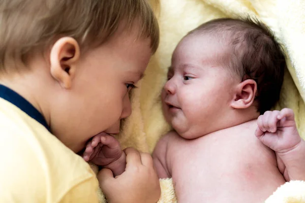 童年、照料、卫生、母性、纯真的概念- -用温暖的黄色毛巾包裹的淋浴后醒着的婴儿与兄妹男孩躺在一起。婴儿第一次洗澡 — 图库照片