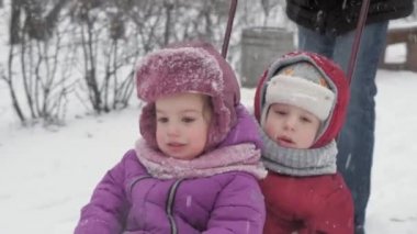 Kış, çocukluk, babalık, oyunlar, aile kavramları - iki mutlu anaokulu çocuğu kardeşler kızakla kayıyor çocuklar babalarıyla birlikte eğleniyor açık havada kar yağışı mevsiminde soğuk havada parkta oynuyorlar.