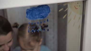 Çocukluk, annelik, yaratıcılık, doğa, sanat, bahar, yaz konsepti - 3-4 yaşlarında küçük kızı olan genç bir annenin pencere camına çizimi. Kadınlar ve anaokulu kızları çiçek boyarlar.