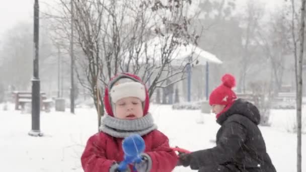Zima, dovolená, hry, rodinné koncepty - Dvě šťastné školky batole děti sourozenci oblečené v klobouky a palčáky s maminkou hrát bavte se, aby sněhová koule na sněžení v chladném období počasí v parku — Stock video