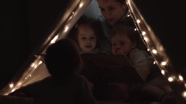 Authentic tender cute mom and preschool kids boy and girl in tent at home. young woman read book to children 2-4 years old in wigwam at night. Family, Childhood, Motherhood, Comfort and Safety concept — Stock Video