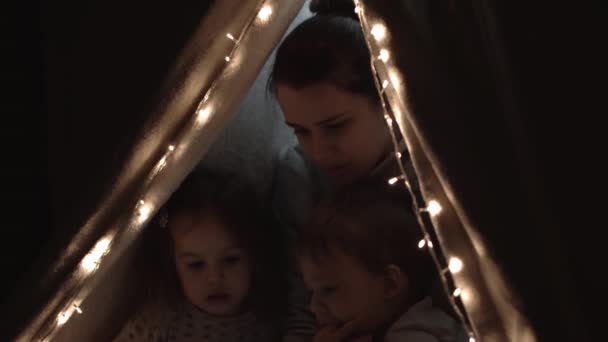 Authentic tender cute mom and preschool kids boy and girl in tent at home. young woman read book to children 2-4 years old in wigwam at night. Family, Childhood, Motherhood, Comfort and Safety concept — Stock Video