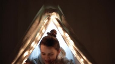 Otantik sevimli anne ve anaokulu çocukları evdeki çadırda kız ve erkek. Genç bir kadın 2-4 yaşlarındaki çocuklara kitap okurdu. Aile, Çocukluk, Annelik, Rahatlık ve Güvenlik kavramı