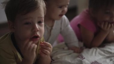 Aile, rahatlık, çocukluk, arkadaşlık kavramları - otantik üç anaokulu çocuğu küçük çocuklar, kardeşler akıllı telefon cihazıyla çizgi film izliyorlar.