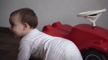 Çocukluk, eğlence, oyunlar, ulaşım, annelik kavramları - küçük mutlu gülümsemeli tombul bebek çocuk 10 ay boyunca büyük oyuncak kırmızı araba scooter 'ı ve evde bip sesi eşliğinde emekleyerek oyna
