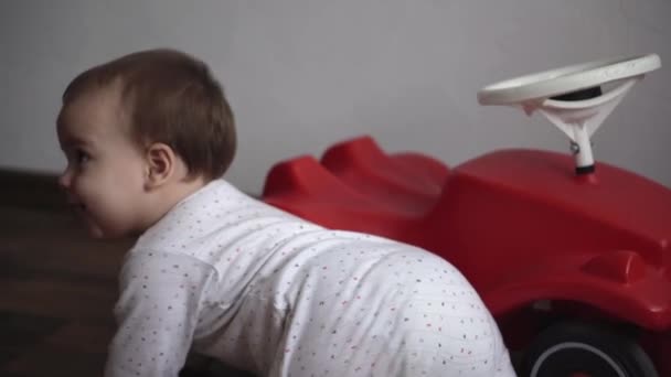 Enfance, divertissement, jeux, transport, concepts de maternité - peu heureux souriant joyeux bébé enfant joufflu enfant 10 mois jouer rampe près de gros jouet scooter de voiture rouge et bips à la maison à l'intérieur — Video