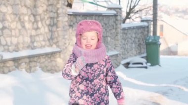 Kış, tatil, oyunlar, aile kavramları. Mor giyinmiş 3-4 yaşındaki küçük kız çocuğu yavaş çekimde buzlu dondurmayı karın üstünde yalıyor. çocuk karlı alanda koşar