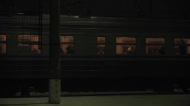 Ulaşım, yol, demiryolu, manzara, yakınlaşma, konsept - gece yarısı tren istasyonundaki trendeki insanları pencereden izlemek. Karlı kışta kırsal bölgelerde demiryolu ile seyahat etmek