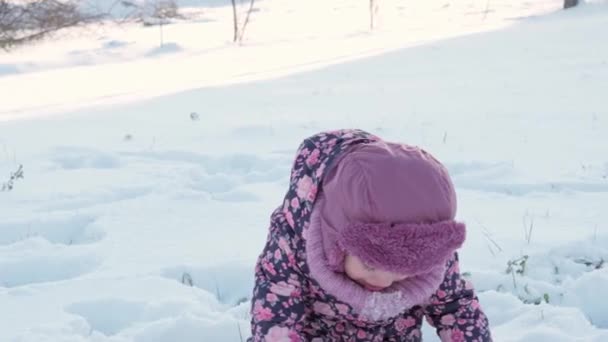 Winter, vacation, games, family concepts - middle plan of authentic little preschool minor 3-4 years old girl in purple on snow-covered meadow plays with snow in countryside. child runs on snowy area — Stock Video