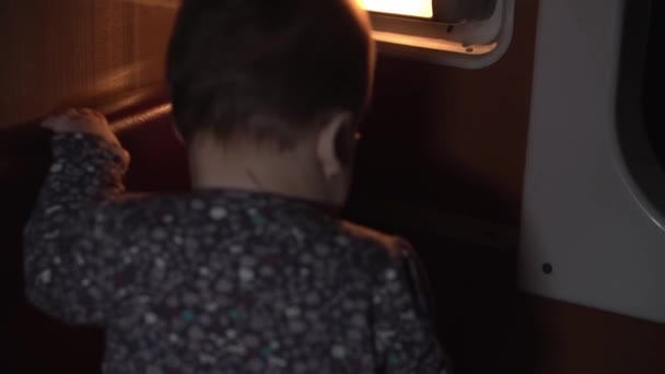 Trasporto, strada, ferrovia, paesaggio, comnicazione, concetto - autentica bambina o ragazzo felice bambino 8-12 mesi che gioca nel buio parziale di un compartimento ferroviario.. viaggiare in campagna in treno — Video Stock