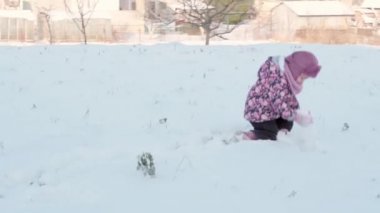 Kış, tatil, oyunlar, aile kavramları. Küçük otantik anaokulu öğrencilerinin orta planı. Kar kaplı çayır üzerinde mor giyen 3-4 yaşındaki kız elleriyle kar kusuyor. çocuk karlı alanda koşar