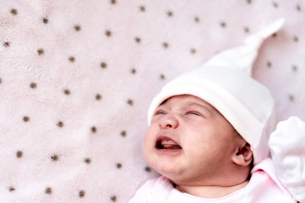 Infanzia, malattia, coliche, gonfiore, maternità, concetti di salute - Close up irrequieto, preoccupato triste neonato ragazza in cappello dorme piangendo urlo hanno mal di stomaco sdraiato sul letto con la bocca aperta — Foto Stock