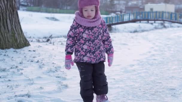 Zima, wakacje, gry, koncepcja rodziny - środkowy plan autentycznego małego przedszkola moll 3-4-letnia dziewczynka w fioletowym kolorze na pokrytej śniegiem łące bawi się śniegiem przed zachodem słońca. dziecko biegnie po śnieżnej okolicy — Wideo stockowe