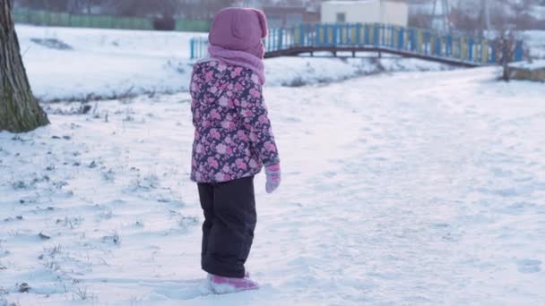 겨울, 휴가, 게임, 가족 컨셉 - 눈덮인 초원에 있는 작은 미취학 아동 3-4 세 소녀가 해 지기 전에 눈을 가지고 노는 모습. 눈덮인 지역에서 아이가 뛰노는 모습 — 비디오