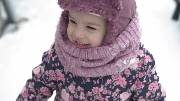 Kış, tatil, oyunlar, aile kavramları - yavaş çekim yakın çekim otantik kız çocuk anaokulu 3-4 yaşlarında kulaklıklı kız çocuğu kar yağışlı havada kamera tebessümlerine bakıyor ve şarkı söylüyor. — Stok video