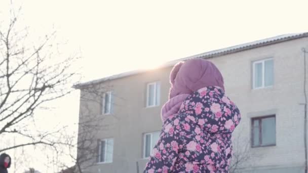 Зима, каникулы, игры, семейные задумки - средний план маленькой дошколячки 3-4 лет в фиолетовом поворачивается лицом к камере и улыбается в подсветке солнца.. ребенок бегает по заснеженной местности — стоковое видео