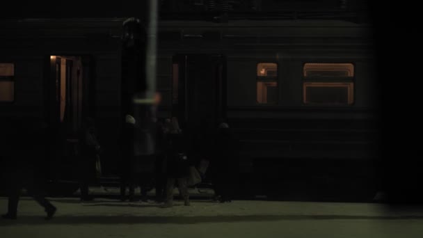 Trasporto, strada, ferrovia, paesaggio, comnication, concetto - vista da finestra su salire a bordo della gente su treno a stazione ferroviaria in crepuscolo di notte. viaggio in campagna in treno in inverno nevoso — Video Stock