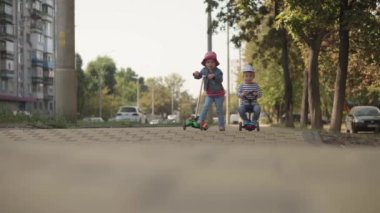 Çocukluk, aile, tatil, ulaşım kavramları. Anaokulu çocukları yaz parkında motosiklet sürerler. Yol kenarında..
