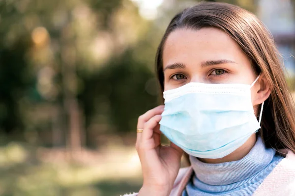Bakım, bebekler, ilkbahar, koronavirüs ve karantina konsepti - Genç, uzun saçlı, Avrupa Kafkasyalı kadın, öğle vakti güneş ışığında mavi tıbbi koruyucu maske takıldı.
