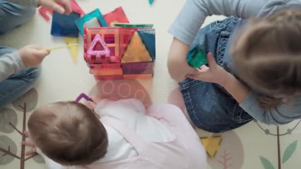 Infanzia, famiglia, concetto di maternità - vista dall'alto giovani felici I bambini amano giocare a magneti di gioco creativi blocchi costruisce castello. Albero I bambini fratelli si divertono insieme in sala giochi in quarantena — Video Stock