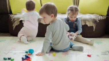 Çocukluk, aile kavramı - üç kardeş çocuk evde eğleniyor. Küçük tatlı çocuklar oyun odasında yerde oyuncak küçük toplarla oynuyorlar. Güzel kız kardeşler kapalı alandaki oyunlardan hoşlanıyor.