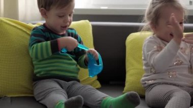 Mavi ve kırmızı sümüklü otantik bebek elleri. Kız ve oğlan anaokulunda yan yana oyun hamuru esnetiyorlar. Çocuk plastikçilik oynuyor. Modaya uygun sıvı oyuncak sarı kanepede el ve parmaklara yapışıyor.