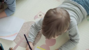 Otantik iki mutlu kardeş yaratıcı çocuklar anneleriyle birlikte kalemle çiziyorlar bahar geliyor resim gökkuşağı içeride, oyun odasında yerde eğleniyor. Çocukluk, Sanat, Eğitim, Yaratıcılık, annelik kavramı