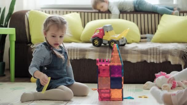 La infancia, la familia, la maternidad, el concepto de paternidad: la joven madre feliz pasa tiempo jugando bloques de imanes construye un castillo con niños pequeños. Alegría Los niños se divierten juntos en el piso de la sala de juegos — Vídeos de Stock