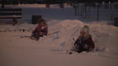Kış, tatil, oyunlar, aile kavramları - otantik, mutlu, küçük anaokulu çocukları akşam parkında eğleniyor, buz gibi havada kartopu heykelleri karların üzerine düşüyor.