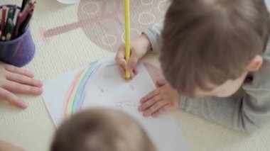 Otantik iki mutlu kardeş yaratıcı çocuklar anneleriyle birlikte kalemle çiziyorlar bahar geliyor resim gökkuşağı içeride, oyun odasında yerde eğleniyor. Çocukluk, Sanat, Eğitim, Yaratıcılık, annelik kavramı